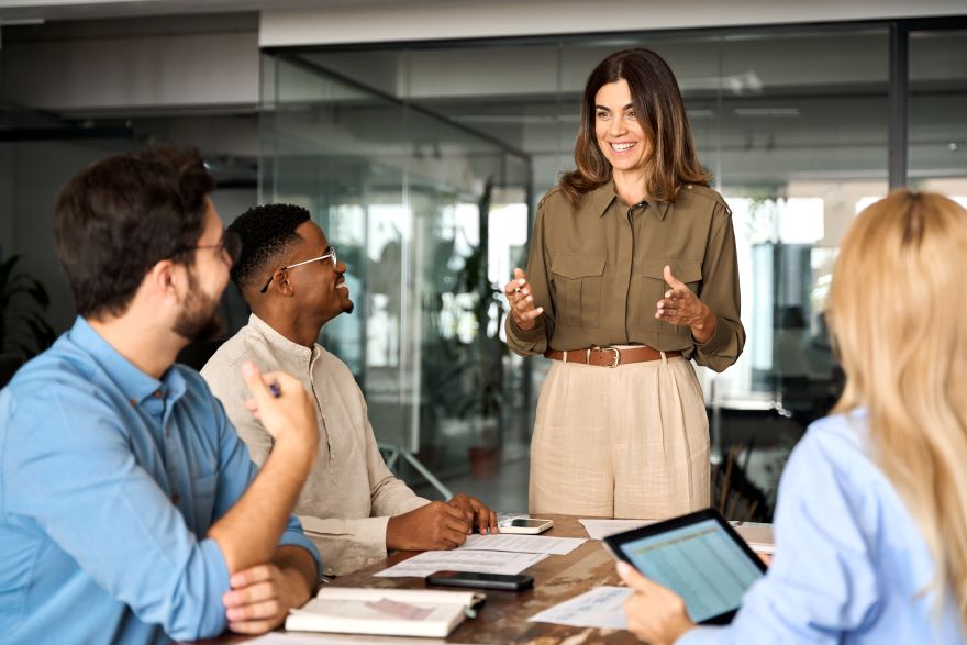 April Marketing Campaigns In Article A woman manager happily talking to work team that is sat around a desk