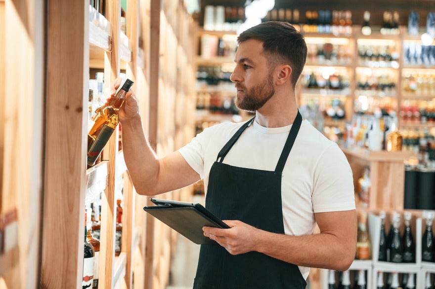 Google Business Profile guidelines Male employee in an apron placing a bottle of alcohol on to a shelf