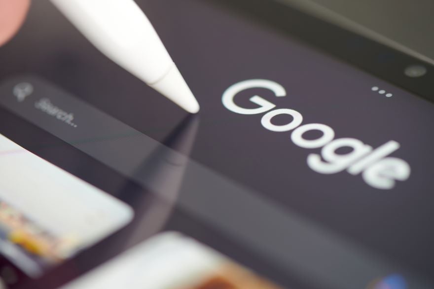 Closeup of a tablet screen with the Google logo and a stylus tapping it