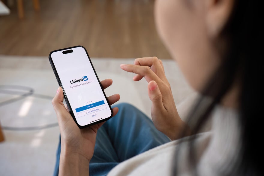 New LinkedIn newsletter metrics Woman holding a mobile phone with the LinkedIn login page on screen