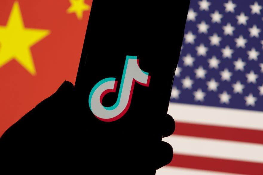 TikTok US Buyer Article Image A hand holding a smartphone displaying the TikTok logo, with a background featuring the flags of China and the USA.